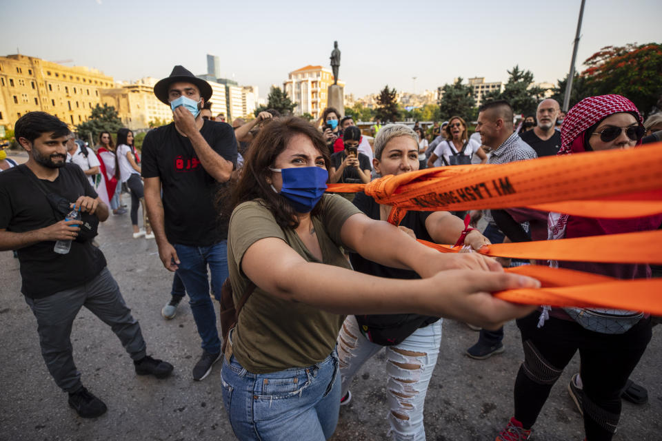 Anti-government protesters try to remove a concrete wall that was installed by security forces to prevent them from reaching the government palace in Beirut, Lebanon, Thursday, July 2, 2020. Major retailers in Lebanon announced Thursday they will temporarily close in the face of an increasingly volatile currency market and their inability to set prices while the local currency tumbles before the dollar. (AP Photo/Hassan Ammar)