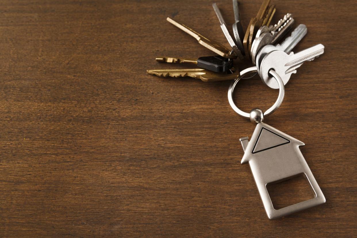 Bunch of keys on a house shaped keychain at wooden table background. Concept for real estate or renting home with copy space