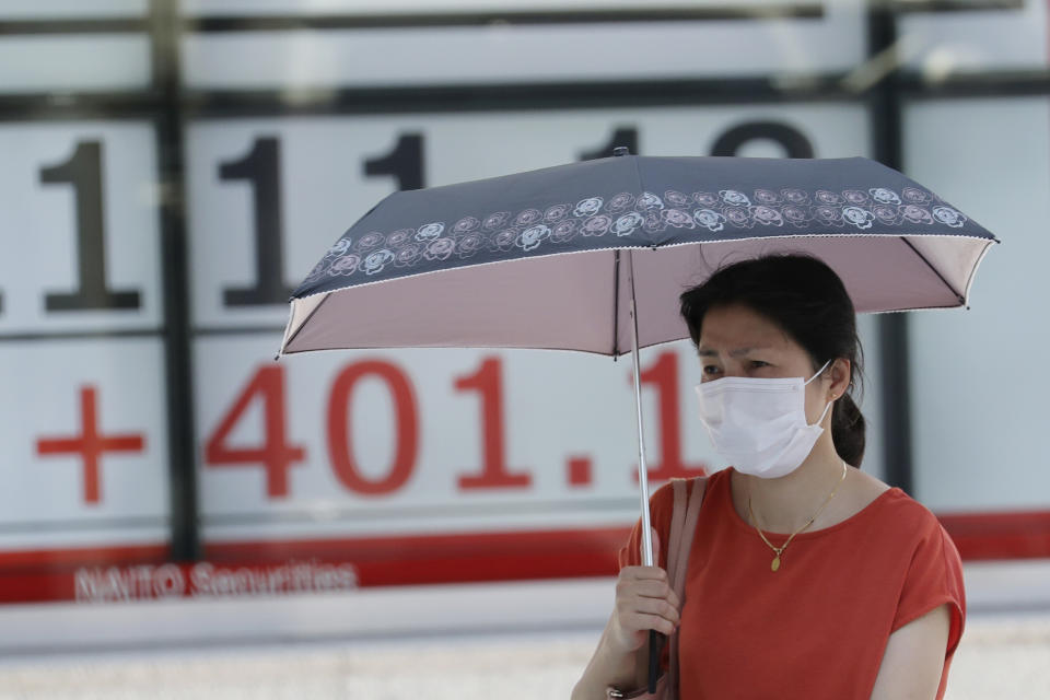 A woman wearing a face mask walks by an electronic stock board of a securities firm in Tokyo, Monday, Aug. 3, 2020. Asian shares were mixed on Monday, as investors watched surging numbers of new coronavirus cases in the region, including in Japan. (AP Photo/Koji Sasahara)