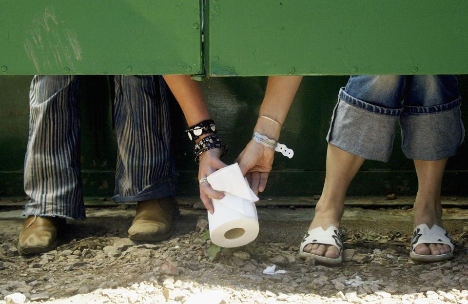 Two festival-goers pass a roll of toilet paper between toilet cubicles in 2004 (Getty Images)