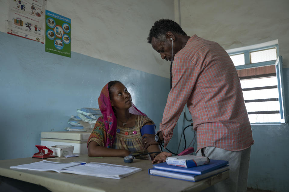 Surgeon and doctor-turned-refugee, Dr. Tewodros Tefera, checks a Tigrayan refugee woman inside the Sudanese Red Crescent (SRC) Clinic, at Hamdeyat Transition Center near the Sudan-Ethiopia border, eastern Sudan, March 17, 2021. (AP Photo/Nariman El-Mofty)