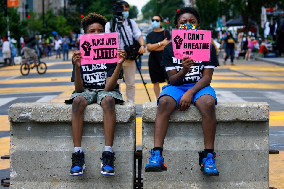 In this June 24, 2020, file photo, Tyshawn, 9, left, and his brother Tyler, 11, right, of Baltimore, hold signs saying "Black Lives Matter" and "I Can't Breathe" as they sit on a concrete barrier near a police line as demonstrators protest along a section of 16th Street that has been renamed Black Lives Matter Plaza in Washington.