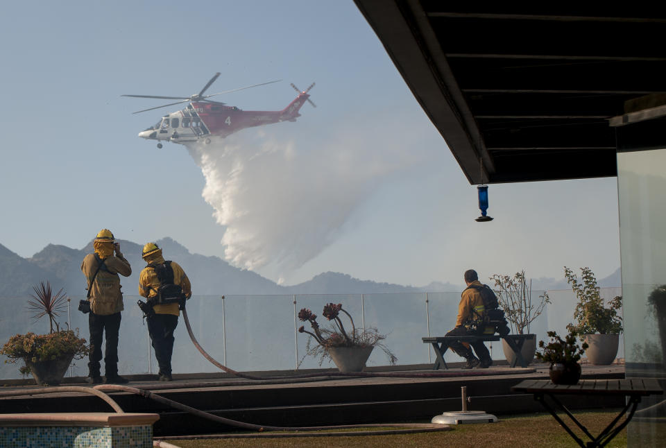 Firefighters watch as a helicopter drops water in a wildfire in the Pacific Palisades area of Los Angeles, Oct. 21, 2019. (AP Photo/Christian Monterrosa)