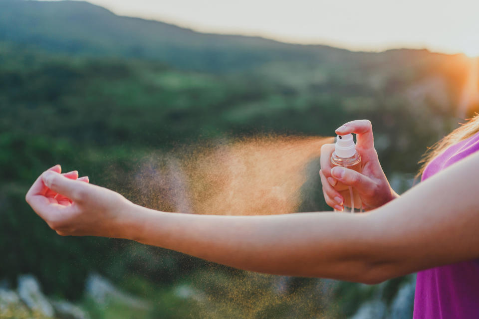 A woman spraying bug spray on her arm