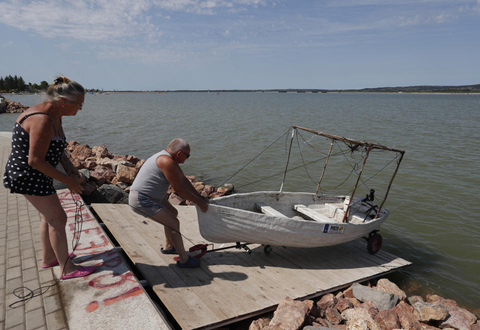 An elderly couple pull their homemade boat from the Lake Velence in Agard, Hungary, Sunday, Aug. 8, 2021. Activists and environmental experts in Hungary say the effects of climate change and insufficient infrastructure are colliding to threaten the country’s third largest natural lake with an economic and ecological crisis. Lake Velence has lost nearly half of its water in the last two years as hot, dry summers have led to increased evaporation and deteriorating water quality. (AP Photo/Laszlo Balogh)