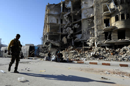 A member of Forces loyal to Syria's President Bashar al-Assad carries his weapon as he walks past damaged buildings in a government held area of Aleppo, Syria December 9, 2016. REUTERS/Omar Sanadiki