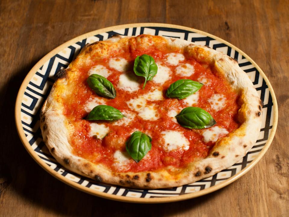 Margherita pizza on a patterned plate with fresh basil.