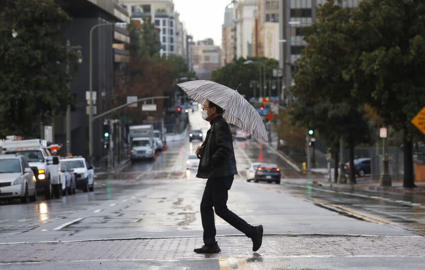 LOS ANGELES, CA - JANUARY 29: Keith Kim crosses Broadway with umbrella in hand as showers lingered into the morning hours in downtown Los Angeles Friday morning after the third cold and wet storm system moves through the Southland.. Downtown on Friday, Jan. 29, 2021 in Los Angeles, CA. (Al Seib / Los Angeles Times).