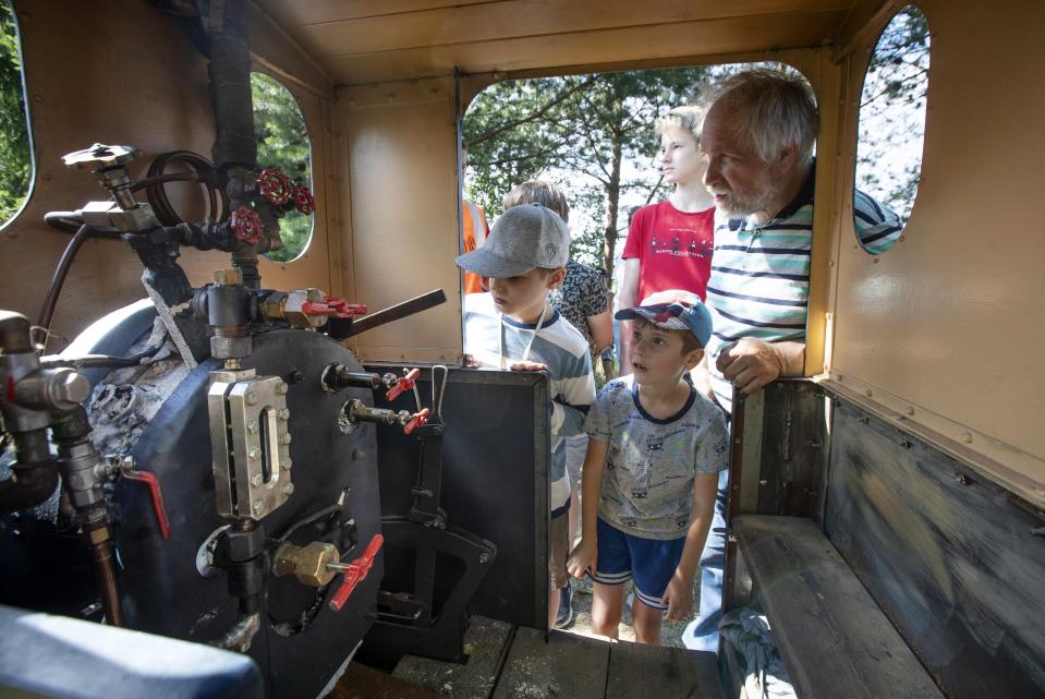 Pavel Chilin explains to children how his steam locomotive works at his miniature personal narrow-gauge railway twisting through the grounds of his home in Ulyanovka village outside St. Petersburg, Russia Sunday, July 19, 2020. It took Chilin more than 10 years to build the 350-meter-long mini-railway complete with various branches, dead ends, circuit loops, and even three bridges.(AP Photo/Dmitri Lovetsky)