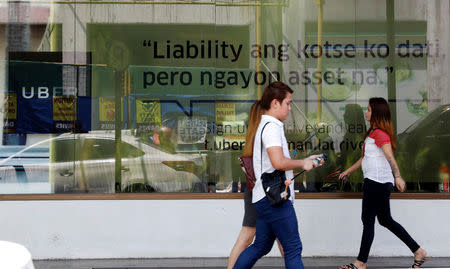 People walk past an Uber advertisement outside the Uber main office in Mandaluyong city, metro Manila, Philippines August 15, 2017. A streamer reads "My car was a liability before but now it's an asset". REUTERS/Dondi Tawatao