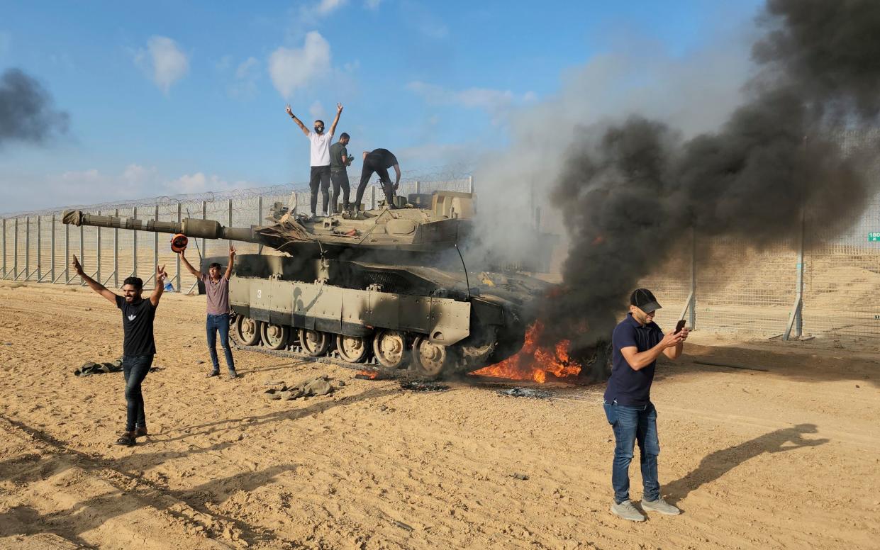 Palestinians celebrate by a destroyed Israeli tank at the Gaza Strip fence east of Khan Younis