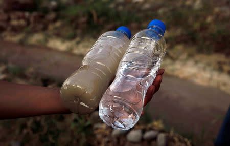 A villager holds two bottles of water, one from a white polluted stream (L), and the other normal mineral water, in Dongchuan district of Kunming, Yunnan province, March 21, 2013. According to local media, the sources of the pollution are production waste water discharged by nearby mining industries as the villagers living around have to use the polluted water for field irrigation and even drinking. Picture taken March 21, 2013. REUTERS/Stringer