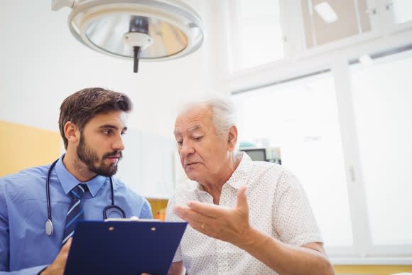 Senior talking to doctor holding clipboard.