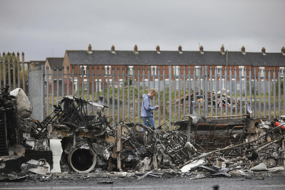 A man walks past a burnt out bus on the Shankill road in West Belfast, Northern Ireland, Thursday, April 8, 2021. The scene follows another night of violence in Loyalist areas that has now spread to interface areas of the peace divide. (AP Photo/Peter Morrison)