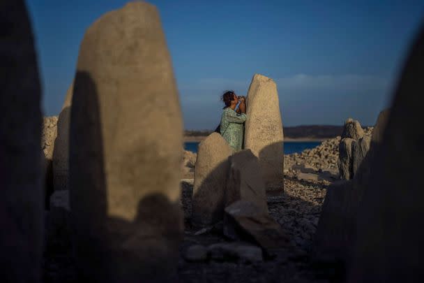 PHOTO: Amalie Garcia picks up her dog next to The Dolmen of Guadalperal, a megalithic monument that emerged due to drought at the Valdecanas reservoir in El Gordo, western Spain, Aug. 13, 2022. (Manu Fernandez/AP)