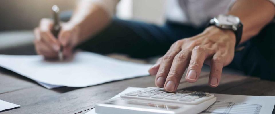 Close up of man's hands using calculator, writing notes with other hand