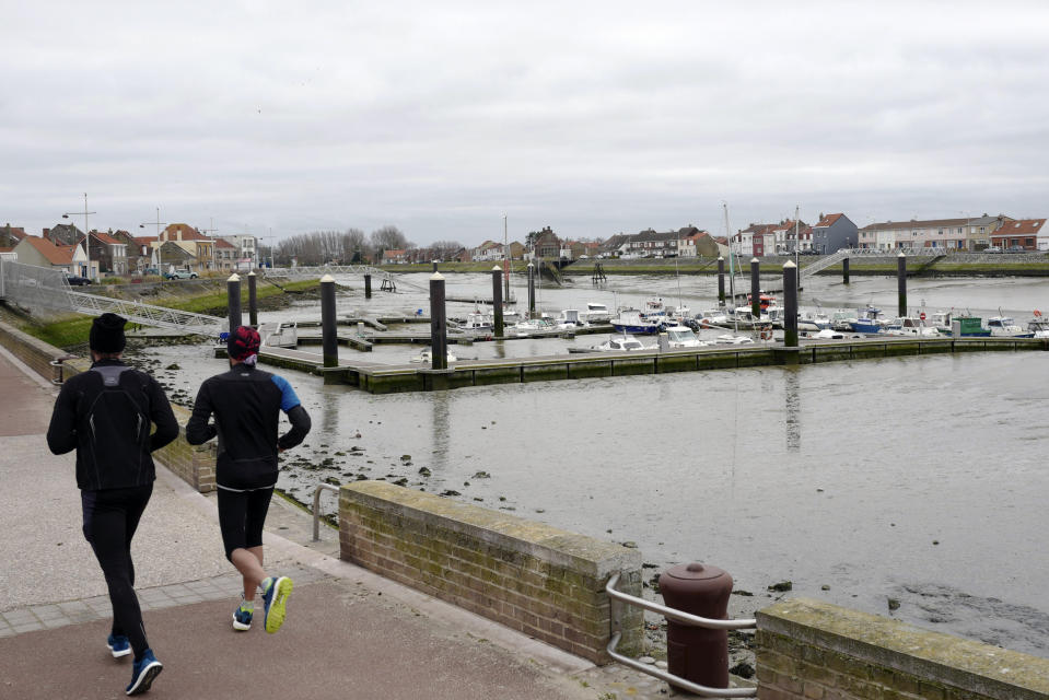 In this photo taken on Wednesday, Jan.16, 2019, joggers run along the port of Oye-Plage, northern France. Land, sea and air patrols are combing the beaches, dunes and frigid, murky coastal waters of northern France in a bid to end an unusual high-risk tactic by migrants, mostly Iranians: trying to sneak across the English Channel in rubber rafts. (AP Photo/Michel Spingler)