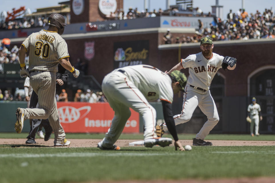 San Francisco Giants relief pitcher John Brebbia, right, watches as Giants first baseman Wilmer Flores (41) bobbles the ball and San Diego Padres' Eric Hosmer (30) reaches during the fourth inning of a baseball game in San Francisco, Sunday, May 22, 2022. (AP Photo/John Hefti)