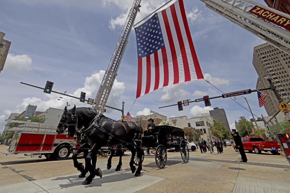 A horse-drawn carriage carries former Louisiana Governor Edwin Edwards under a giant American flag on North 4th Street in Baton Rouge, La., Sunday, July 18, 2021. A processional featuring a law enforcement motorcade and the Southern University Marching Band was held though the streets of downtown Baton Rouge, ending at the Old State Capital building where a private funeral service was held. The colorful and controversial four-term governor died of a respiratory illness on Monday, July 12th at the age of 93. (AP Photo/Michael DeMocker)