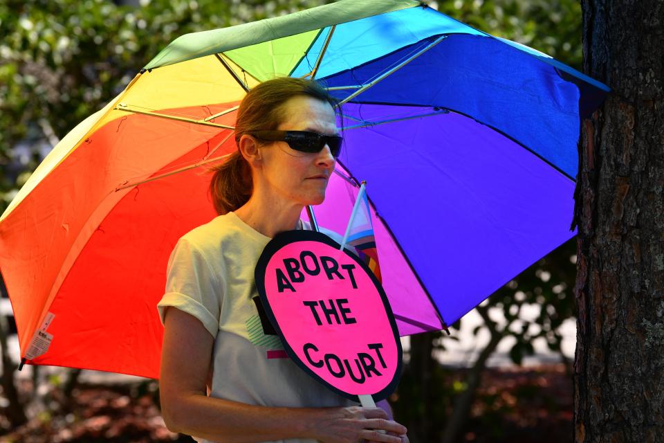 Leann Chaney holds and an "Abort the Court" sign while listening to speakers and standing under a rainbow umbrella during the Fourth of July protest in Viera.