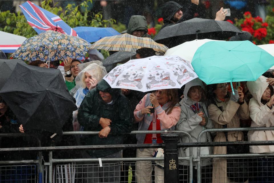 Crowds take cover under umbrellas as they wait for the balcony appearance (Getty Images)