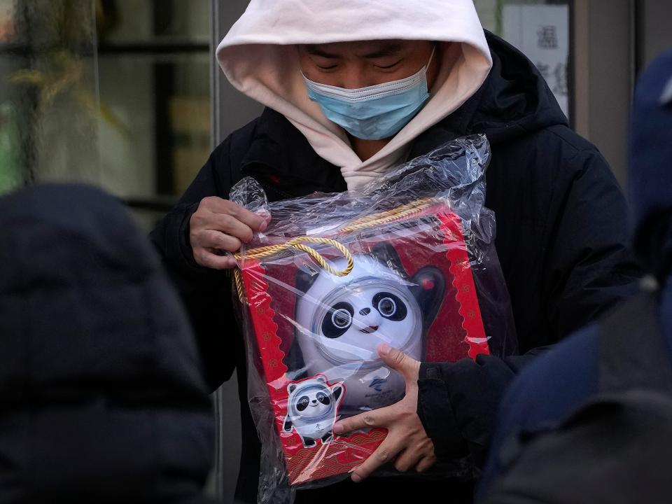 A man holds the Olympic mascot Bing Dwen Dwen doll which he purchased from a store selling 2022 Winter Olympics memorabilia in Beijing, Monday, Feb. 7, 2022. The race is on to snap up scarce 2022 Winter Olympics souvenirs. Dolls of mascot Bing Dwen Dwen, a panda in a winter coat, sold out after buyers waited in line overnight in freezing weather.