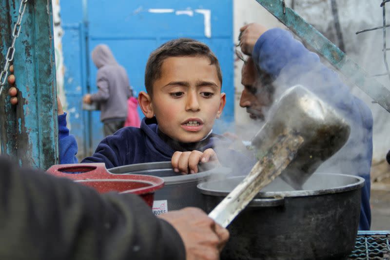 Un niño palestino espera para recibir una comida gratuita compuesta de Khobiza, una verdura de hoja silvestre, durante el mes sagrado del Ramadán, en medio del actual conflicto entre Israel y Hamás, en Jabalia, en el norte de la Franja de Gaza