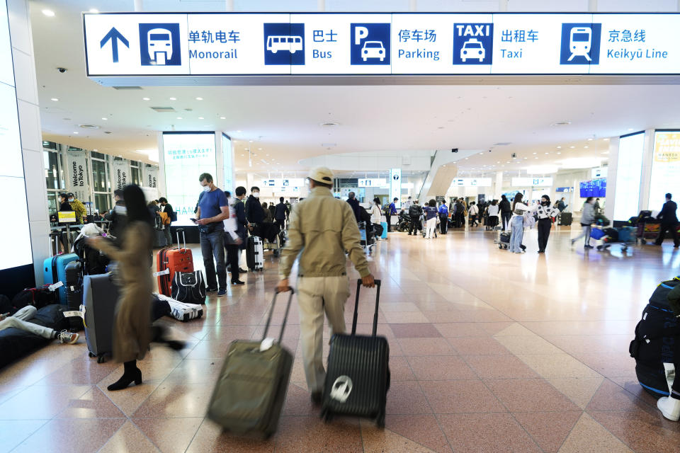 Flight passengers walk through an arrival floor past Chinese and English signs indicating transportations to leave the Haneda International Airport in Tokyo on Jan. 14, 2023. A hoped-for boom in Chinese tourism in Asia over next week’s Lunar New Year holidays looks set to be more of a blip as most travelers opt to stay inside China if they go anywhere. (AP Photo/Hiro Komae)