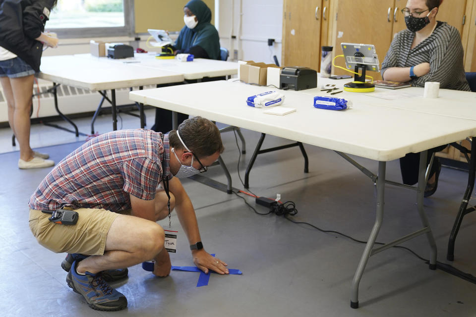 Election judge Tyler Sahnow uses tape to mark off spots on the floor for voters to stand before the voters arrive to cast their ballots at Northeast Middle School in Minneapolis, Minnesota, during the first election in Minnesota since the full outbreak of the COVID-19 pandemic, Tuesday, Aug. 11, 2020. (Anthony Souffle/Star Tribune via AP)