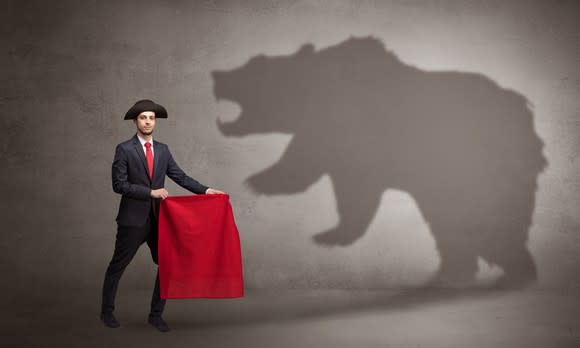 A businessman dressed as a matador tempts the shadow of a bear.