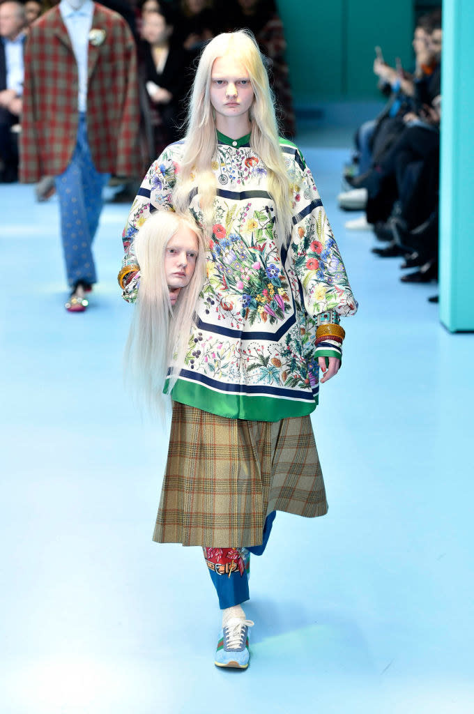 A model on the runway carrying a head that looks like them