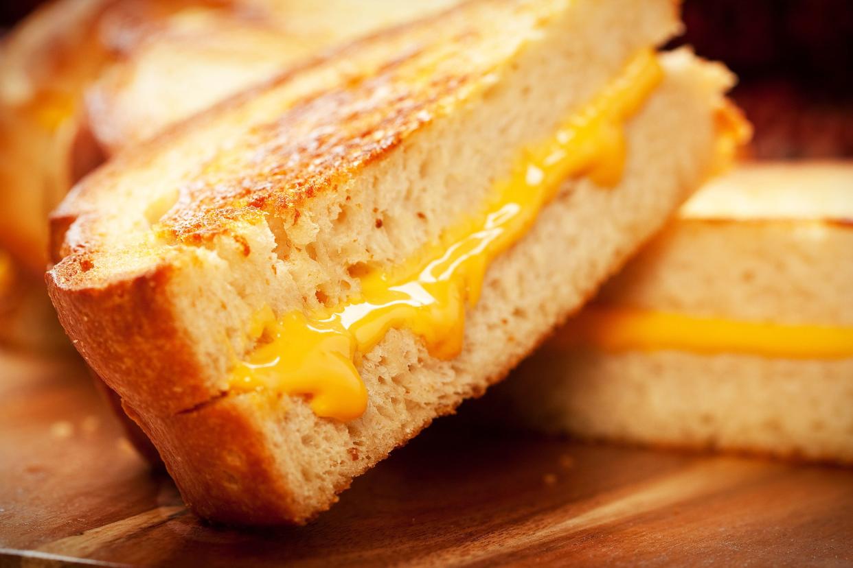 Closeup of grown up grilled cheese sandwich slice on another slice on an artistic wooden cutting board with a blurred background of more slices