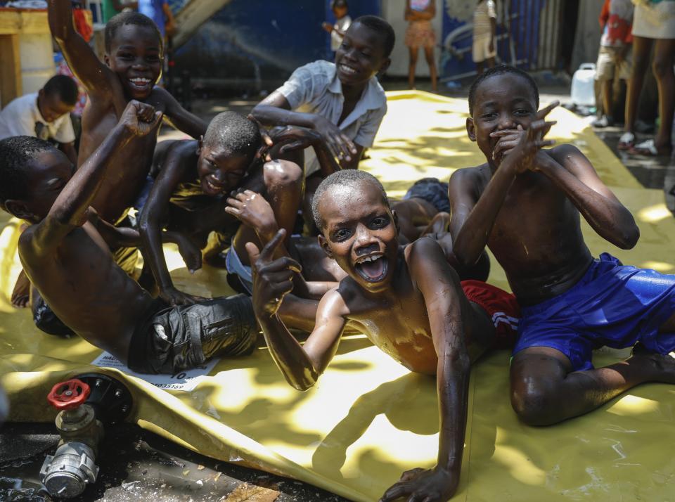 Children react to the camera as they play on a slip-and-slide at a shelter for families displaced by gang violence, in Port-au-Prince, Haiti, Friday, March 22, 2024. (AP Photo/Odelyn Joseph)