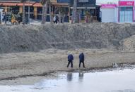 People walk past a huge sand shaft built to protect the Arenal Beach ahead of the upcoming storm "Gloria", in Javea near Alicante