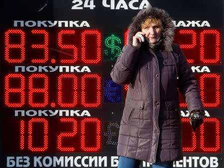 FILE PHOTO: A woman uses a mobile device near a board showing currency exchange rates of the U.S. dollar, Euro and the British pound against the rouble in Moscow, Russia, January 21, 2016. REUTERS/Sergei Karpukhin/File Photo