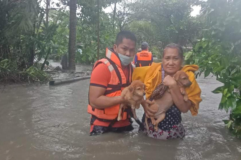 In this handout photo provided by the Philippine Coast Guard, a rescuer helps a woman carry her puppies along floodwaters caused by tropical storm Conson in Naic, Cavite province, Philippines on Wednesday Sept. 8, 2021. Typhoon Conson on Tuesday slammed into the eastern Philippines, causing power outages, suspension of work in government offices, and flooding in some areas. The weather bureau later downgraded it to a tropical storm. (Philippine Coast Guard via AP)