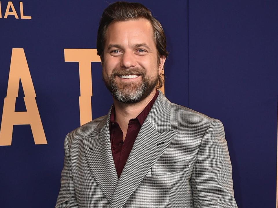 Joshua Jackson smiles for photos on the red carpet in a patterned suit and burgundy shirt.