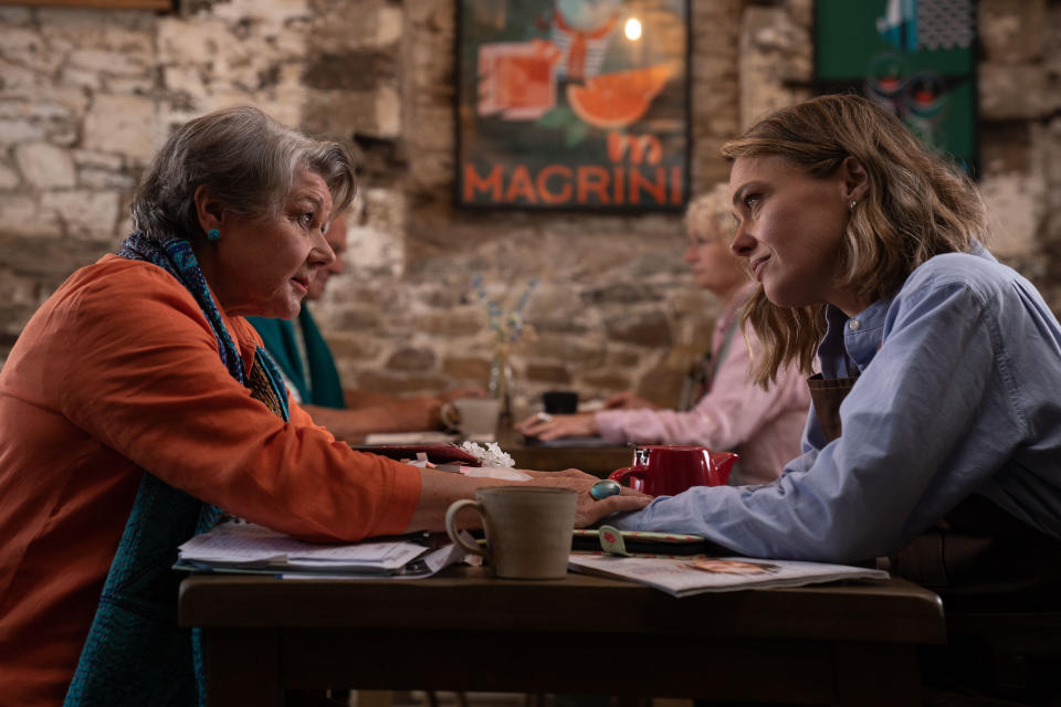 Anne (Barbara Flynn) and Martha (Sally Bretton) sit at opposite sides of a table in Ten Mile Kitchen. Anne is reaching across and has placed her hands on top of Martha's.