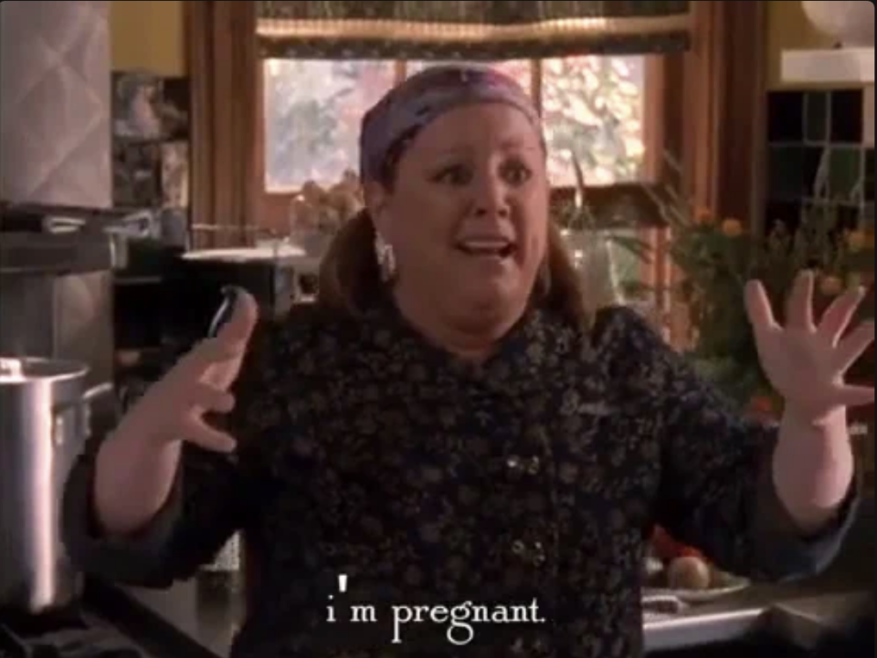 A woman in a kitchen is surprised, gesturing with her hands. Subtitles read, "I'm pregnant."