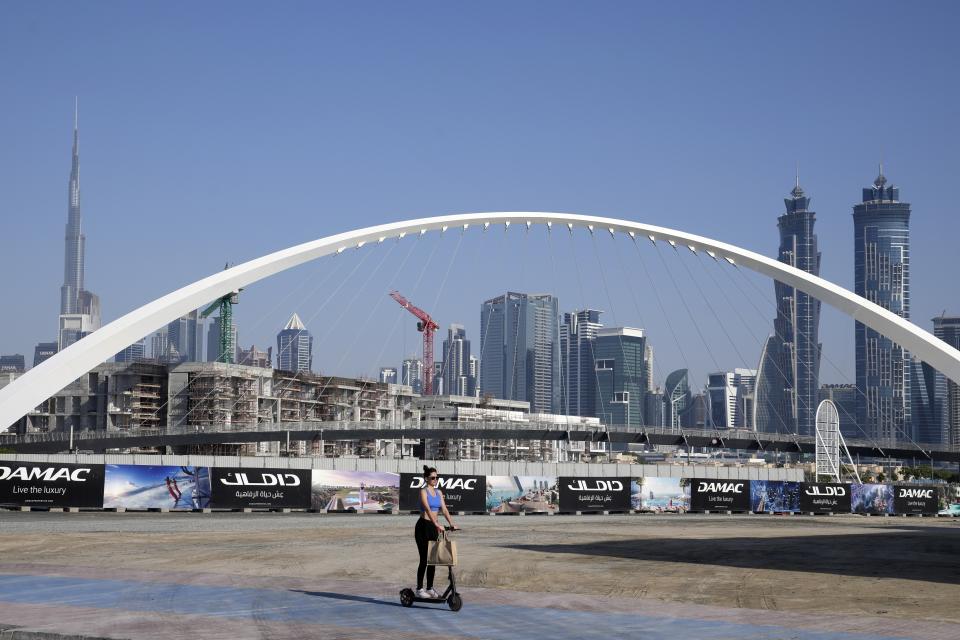 A woman rides a scooter while passing by the advertising billboards of a new residential project in Dubai, United Arab Emirates, Tuesday, Jan. 31, 2023. For the first time since a 2009 financial crisis nearly brought Dubai to its knees, several major abandoned real estate projects now show signs of life. As with its other booms, war again is driving money into Dubai and buoying its economy. This time it's Russian investors fleeing Moscow’s war on Ukraine, rather than people escaping Mideast battlefields. (AP Photo/Kamran Jebreili)