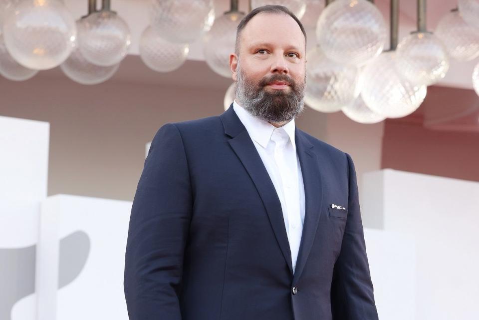 director yorgos lanthimos at poor things event at 2023 venice international film festival, he has grey hair and a thick grey beard and wearing a dark suit jacket, as he stands in front of some spherical lights