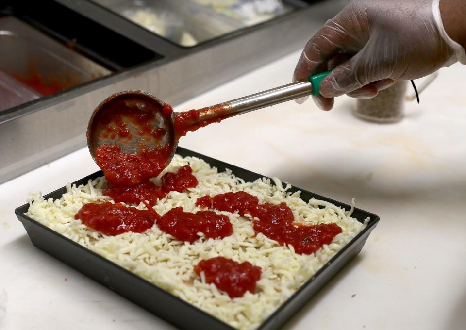 Kendrick Hall adds sauce on top of the cheese of a Detroit pizza at Squirrel's Pizza at the Eastern Wharf.