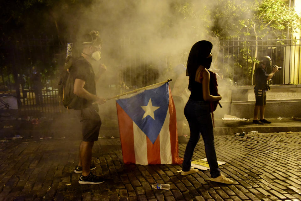 Demonstrators with a flag of Puerto Rico are under the tear gas thrown by the police during clashes near the executive mansion demanding the resignation of Gov. Ricardo Rossello, in San Juan, Puerto Rico, Wednesday, July 17, 2019. (Photo: Carlos Giusti/AP)