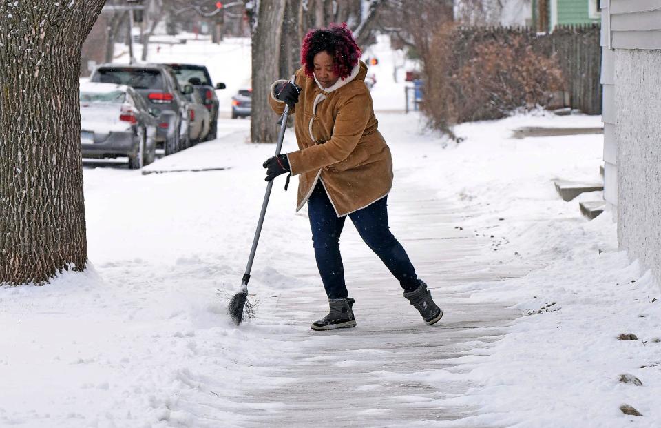 A woman sweeps the sidewalk of snow at the International Church Thursday, March 21, 2024 in Bismarck, N.D (AP)