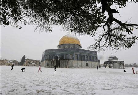 People walk in front of the snow capped Dome of the Rock in the compound known to Muslims as Noble Sanctuary and to Jews as Temple Mount, in Jerusalem's Old City December 12, 2013. REUTERS/Ammar Awad