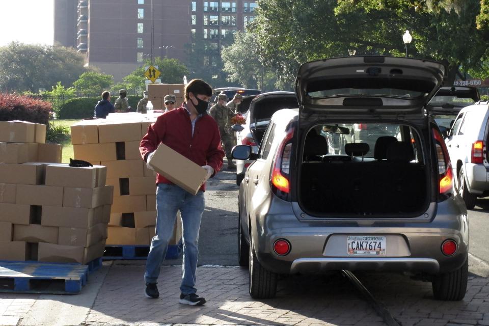 A man wearing a mask loads a box of food into the back of an SUV in Savannah, Ga., as jobless workers lined up in their cars at a drive-thru food bank on Thursday, April 16, 2020. Savannah business leaders and a local charity arranged the drive-thru food bank to help hospitality industry workers left jobless as the coronavirus has virtually shut down Savannah's $3 billion tourism economy. (AP Photo/Russ Bynum)