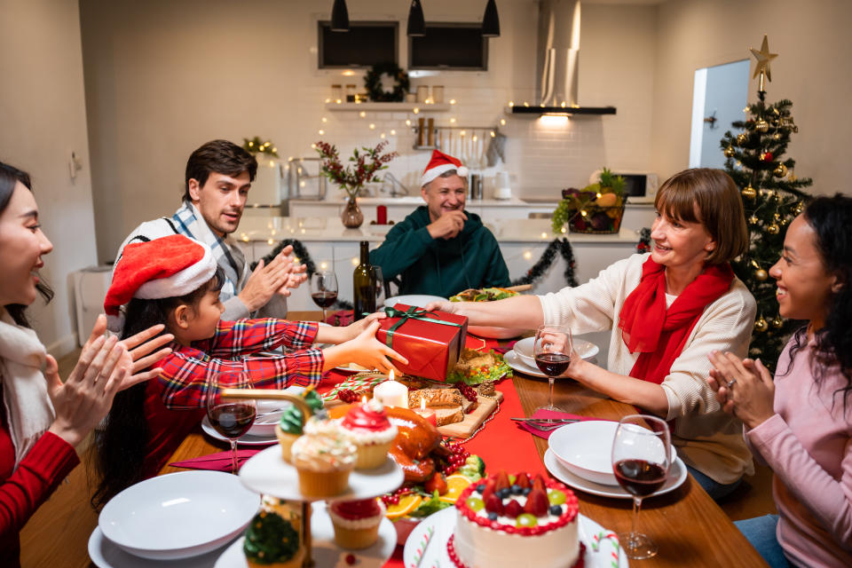 Family enjoying Christmas dinner at home, handing present to kid at the table. (Getty Images)