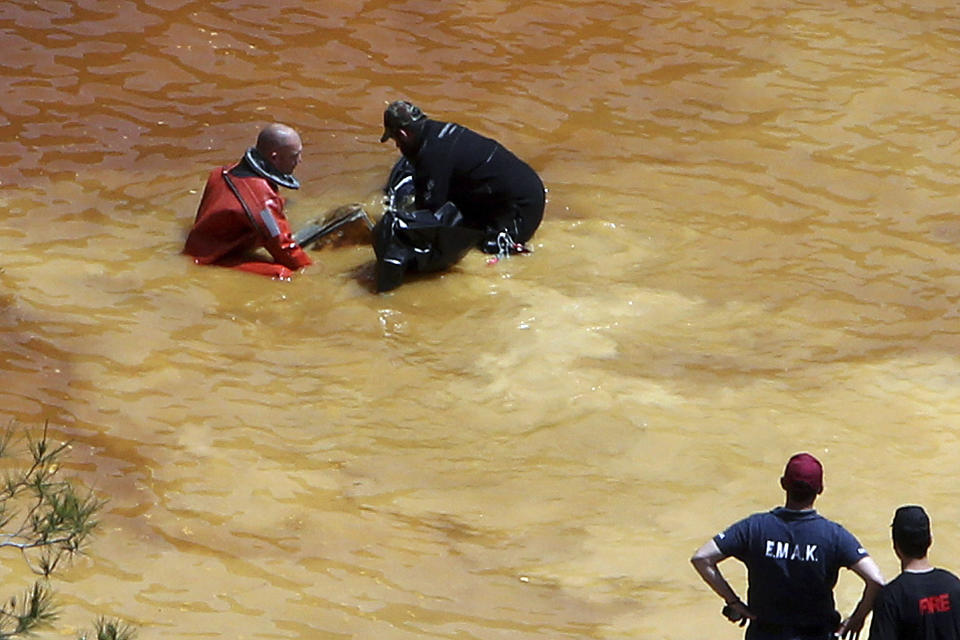 FILE - In this Sunday, April 28, 2019 file photo, a diver, left, and an Investigator remove a suitcase found in a man-made lake, near the village of Mitsero outside of the capital Nicosia, Cyprus. A Cyprus criminal court on Monday, June 24, 2019, has sentenced an army captain Nicholas Metaxas, 35, to seven life terms in prison after he pleaded guilty to the premeditated murder and kidnapping of seven foreign women and girls. (AP Photo/Petros Karadjias, File)