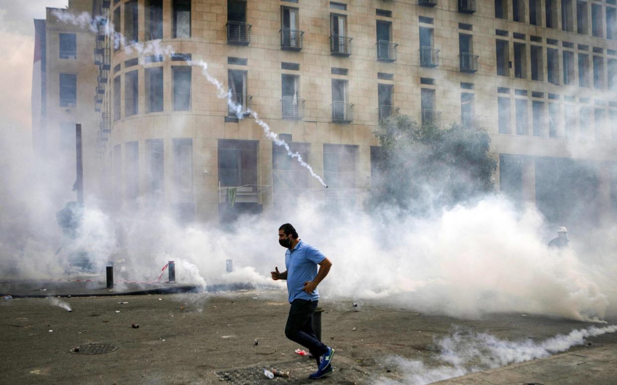 A Lebanese protester runs for cover from tear-gas fired by security forces during clashes in downtown Beirut following demonstrations over the explosion which ripped through the city - Patrick Baz /AFP