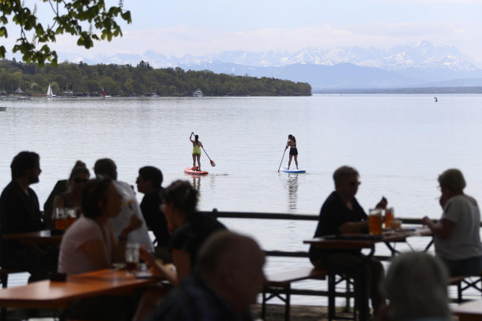 Stand-up paddler make their way while people enjoy the sunny weather on the re-opening day of beer gardens, following the lifting of measures to avoid the spread of the corona virus, at lake 'Ammersee' in front of the alps in Inning, Germany, Monday, May 10, 2021. (AP Photo/Matthias Schrader)